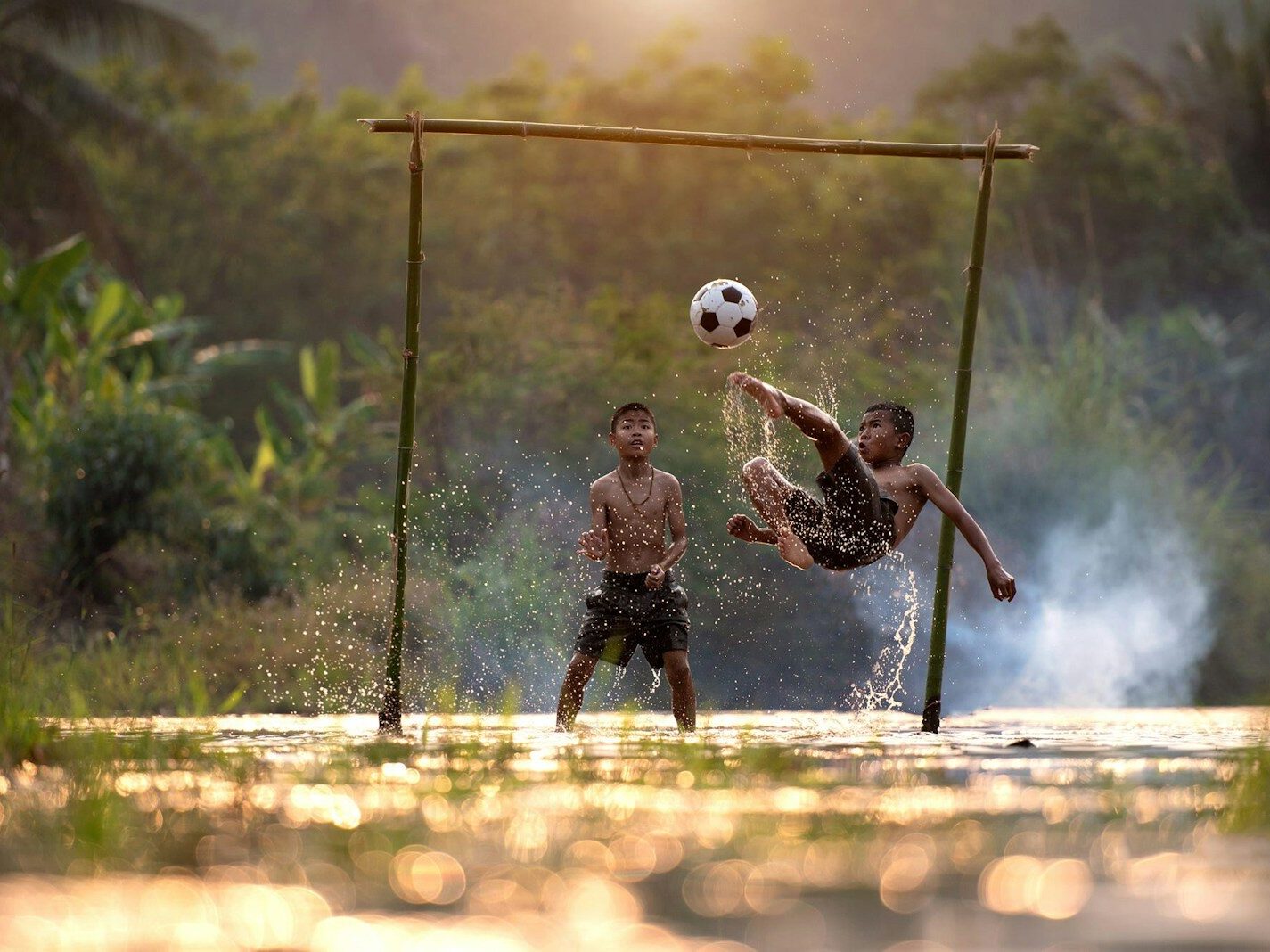 2 boys playing soccer on water during daytime