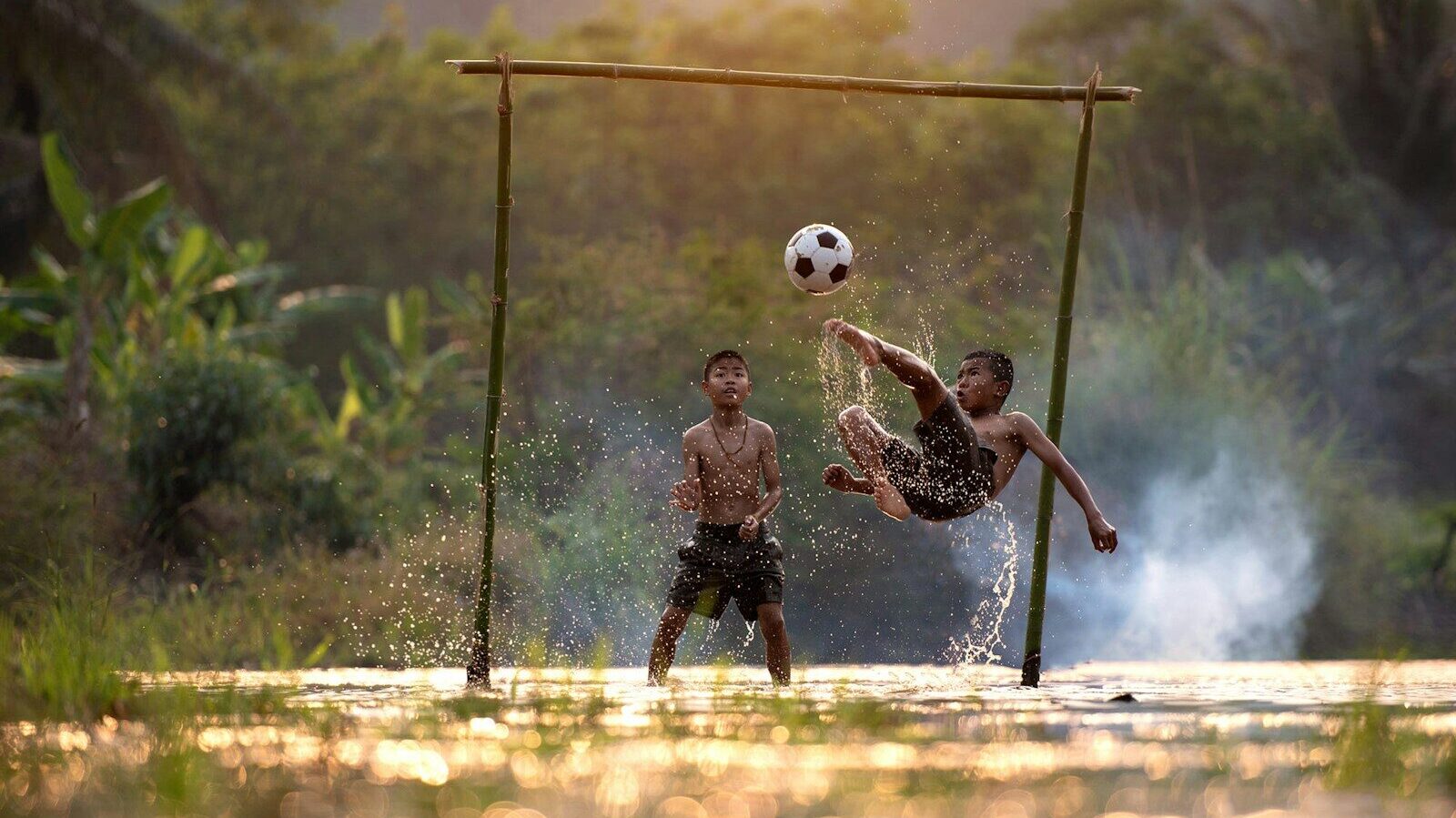 2 boys playing soccer on water during daytime